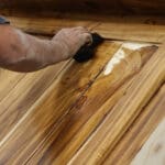 Professional applying wood stain to a wood door, showing the grain-enhancing results of expert wood staining in Baton Rouge.