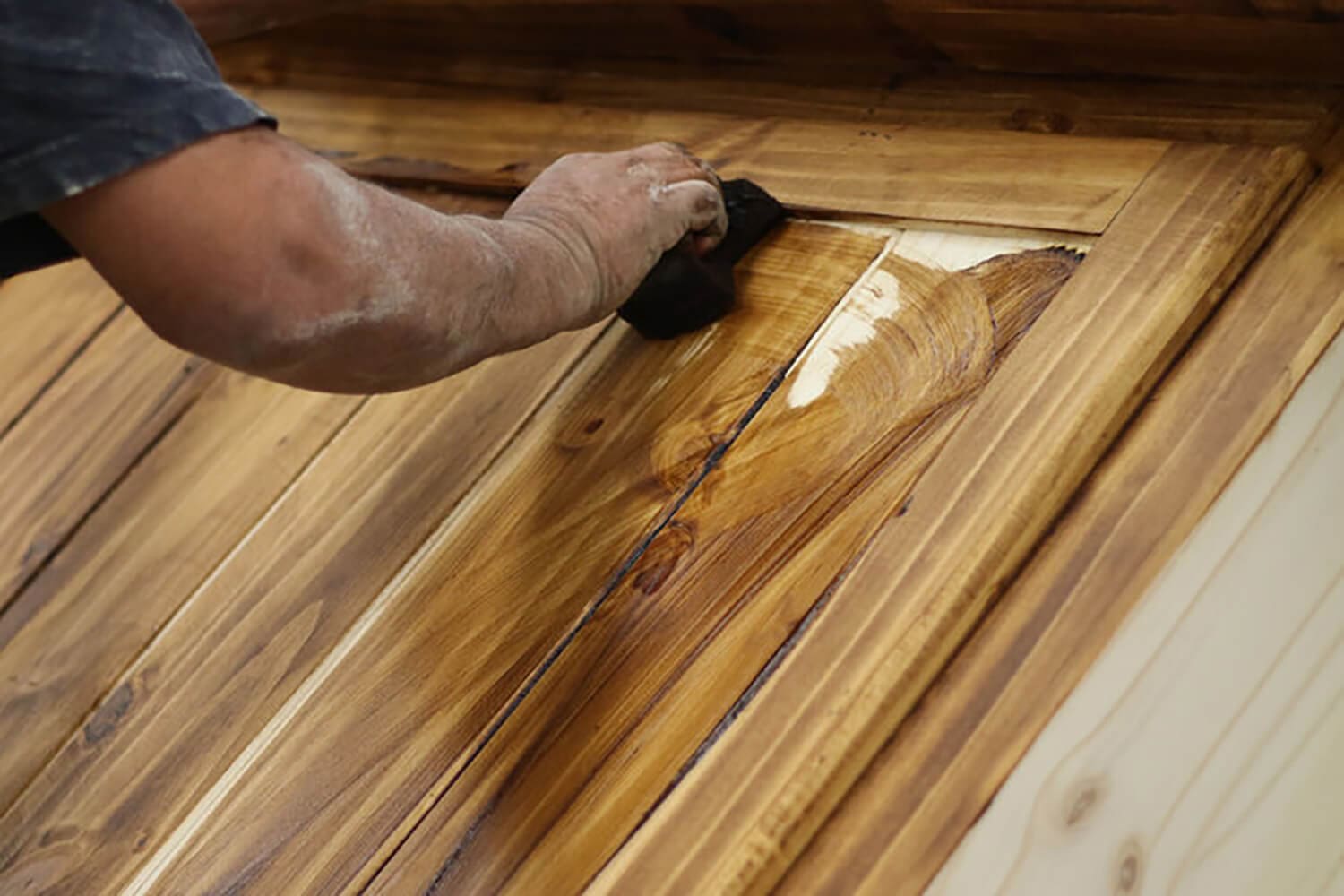 Professional applying wood stain to a wood door, showing the grain-enhancing results of expert wood staining in Baton Rouge.