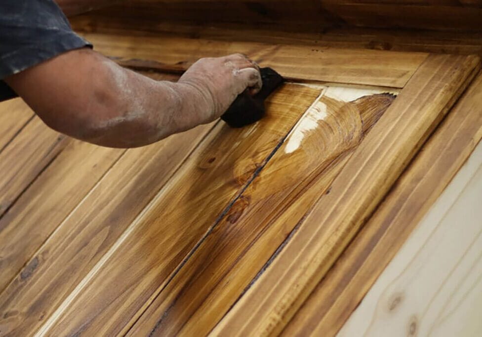 Professional applying wood stain to a wood door, showing the grain-enhancing results of expert wood staining in Baton Rouge.